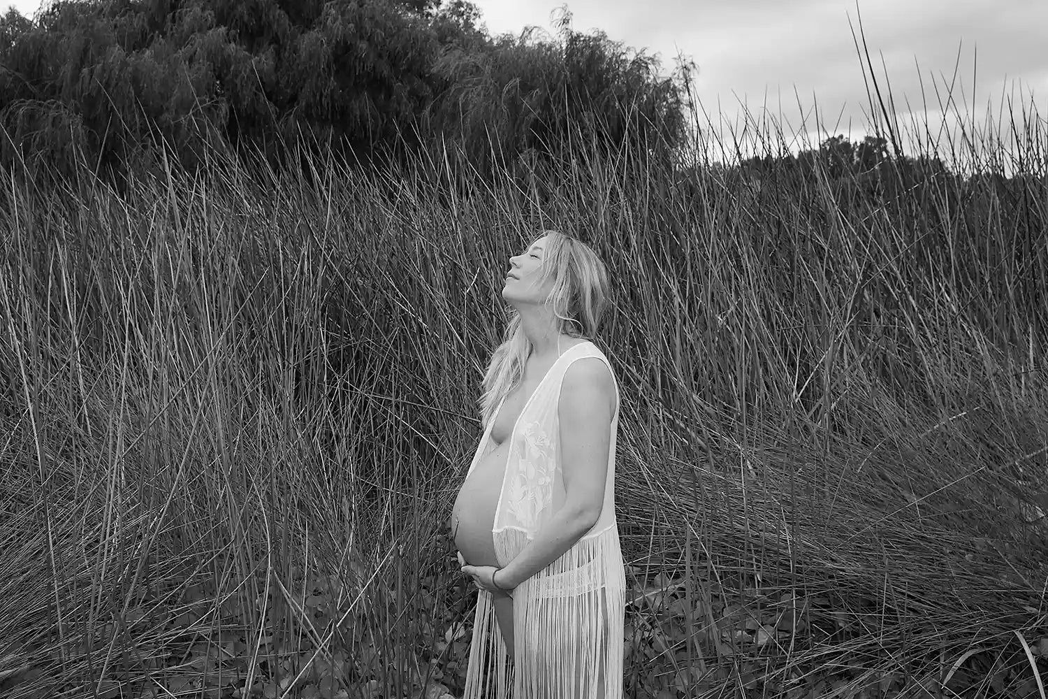 Pregnant woman standing in tall grass, black and white photo